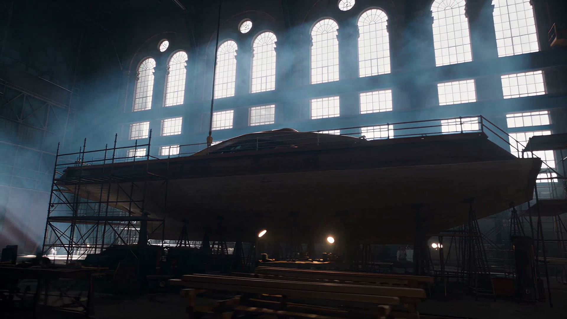 The hull on staging inside the shed, backlit by the arched windows.